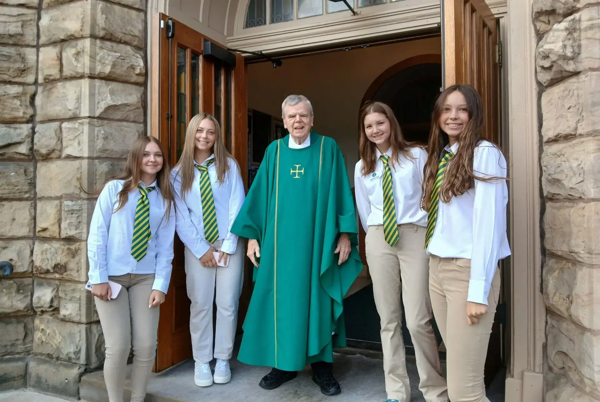 STVM students standing by open doors with a member of the clergy wearing green liturgical vestments.