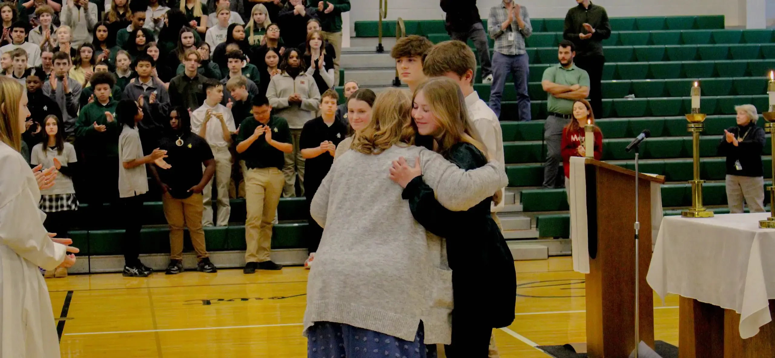 STVM student giving a teacher a hug during a religious service at school while other students applaud.