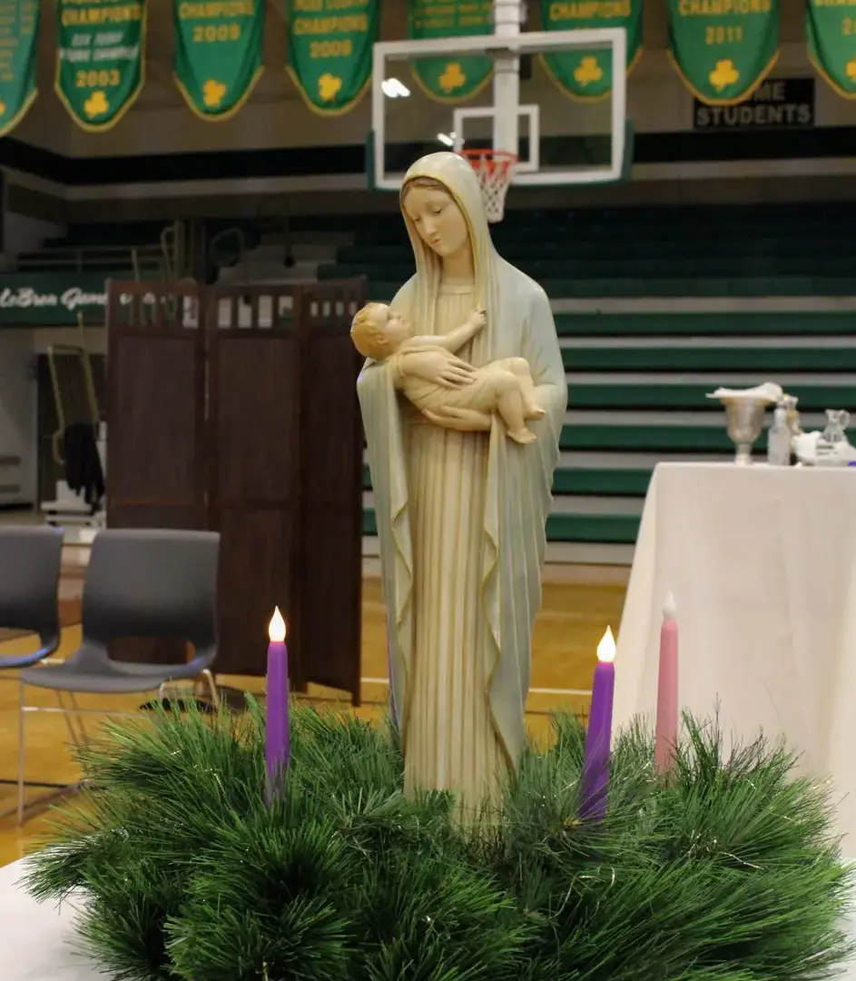 Statuette of St. Mary and the infant Jesus surrounded by candles and a wreath.
