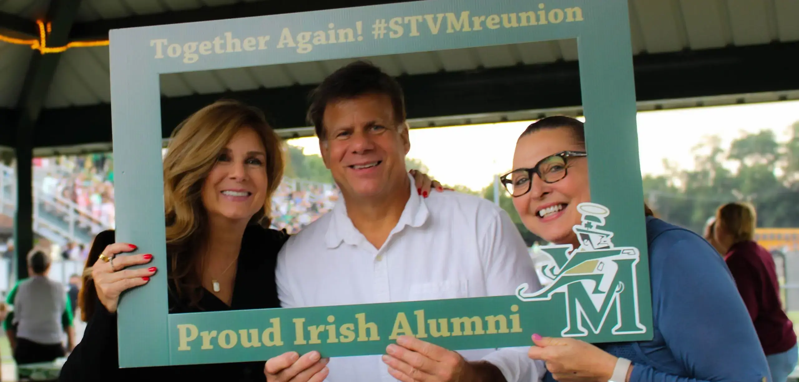 St Vincent St Mary High School alumni smiling for a photograph, holding a frame reading 'Proud Irish Alumni'.