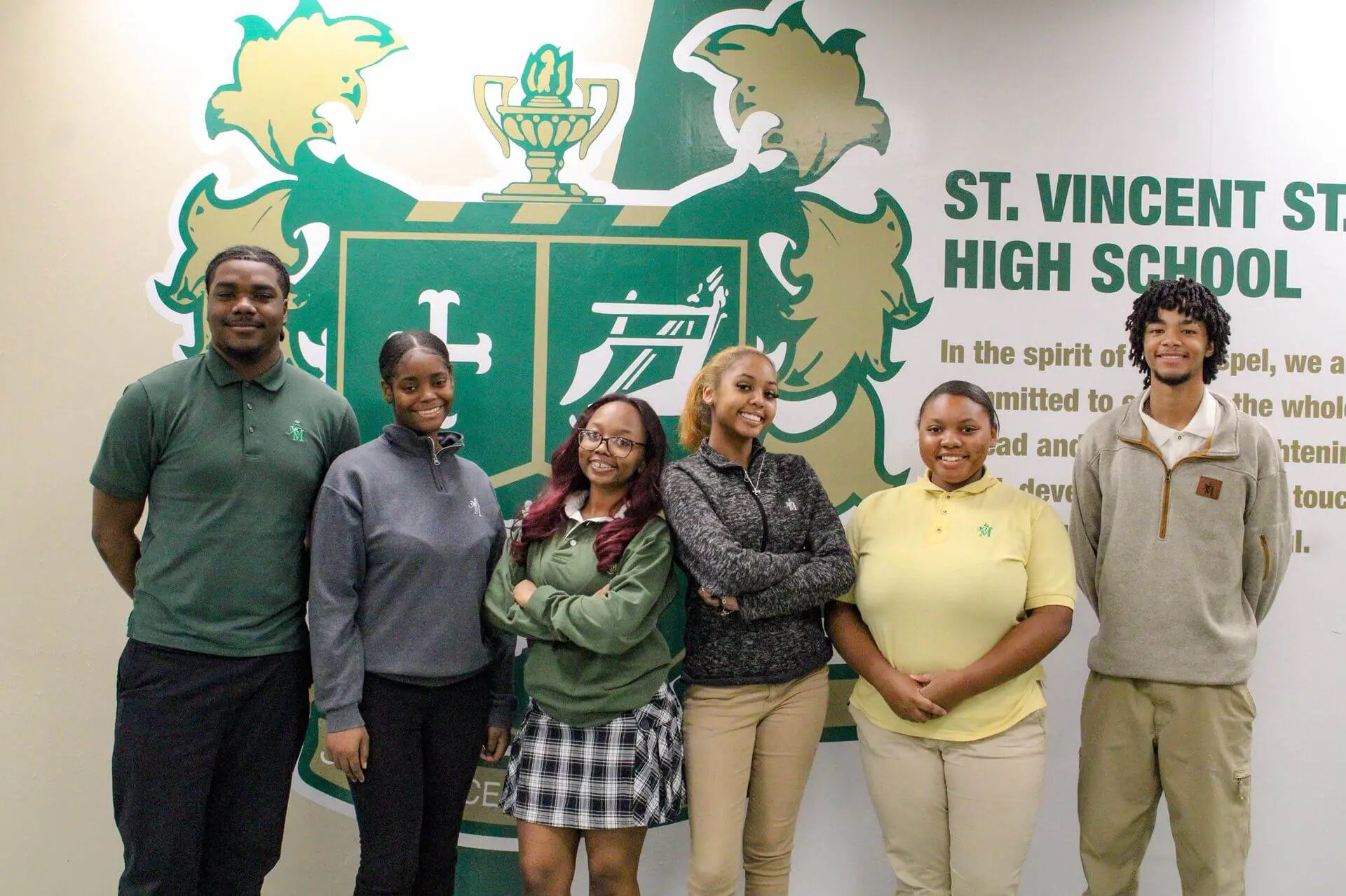 STVM students standing by a mural of the school crest, smiling joyfully.