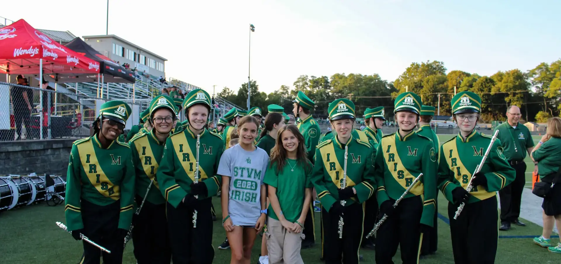 STVM marching band members with Club Irish attendees on the athletics field.