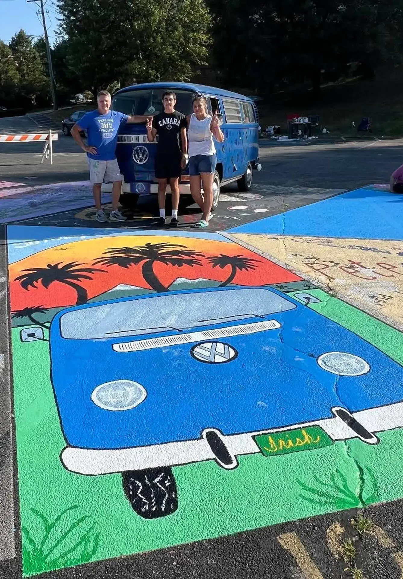 St. Vincent-St. Vincent St. Mary High School students and parents standing by a senior parking spot painted with a van, palm tress, & a sunset.