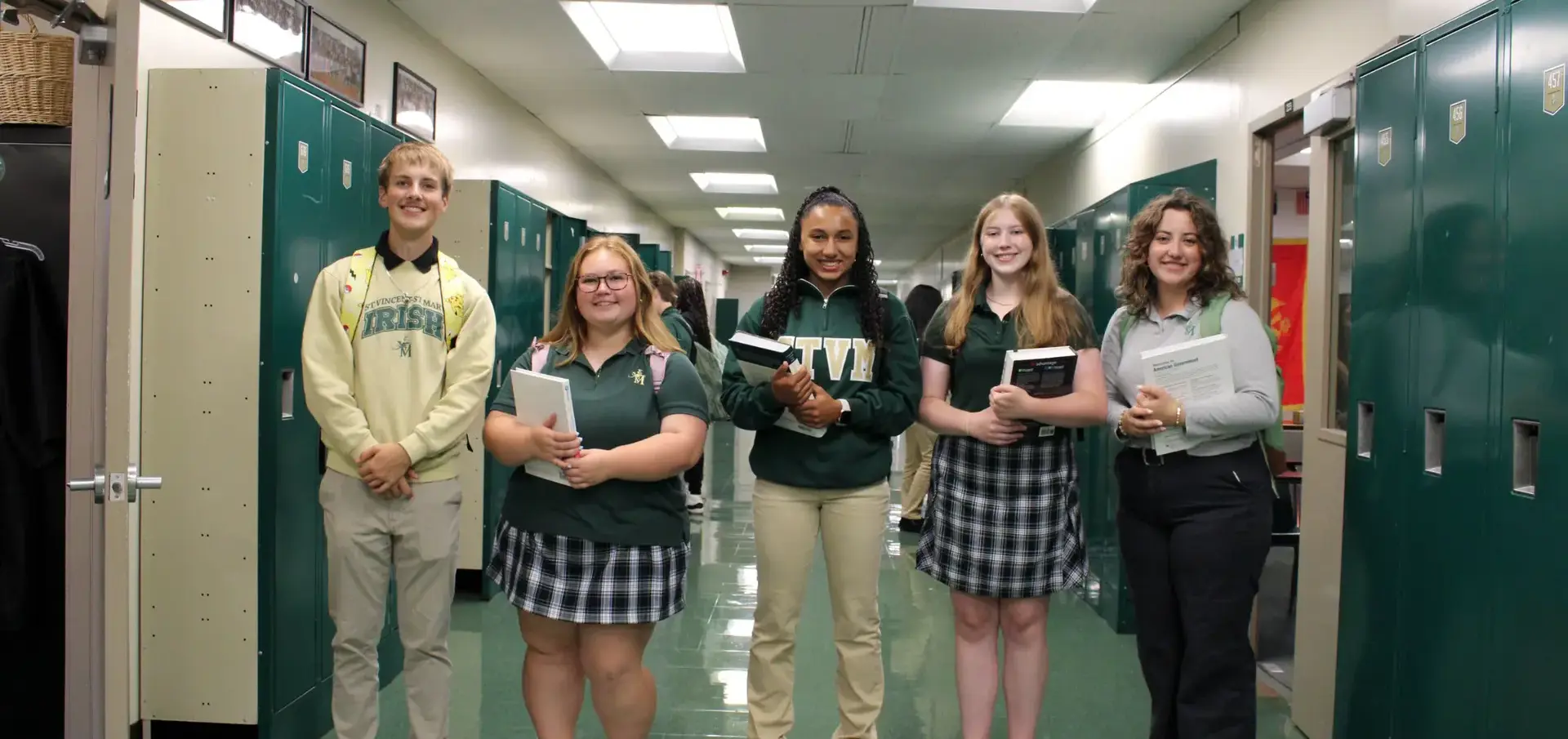 STVM students by their lockers int he hallway, holding books, smiling joyfully.