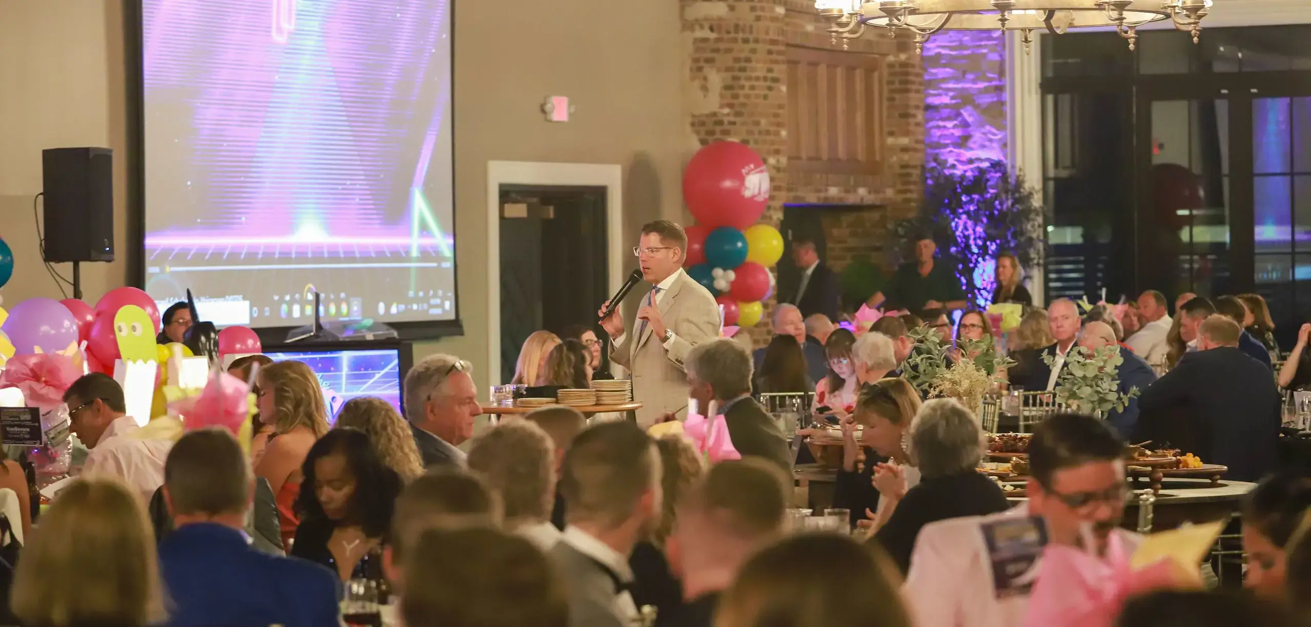 STVM Showcase attendees listening to event speaker, sitting at round dining tables decorated with balloons.