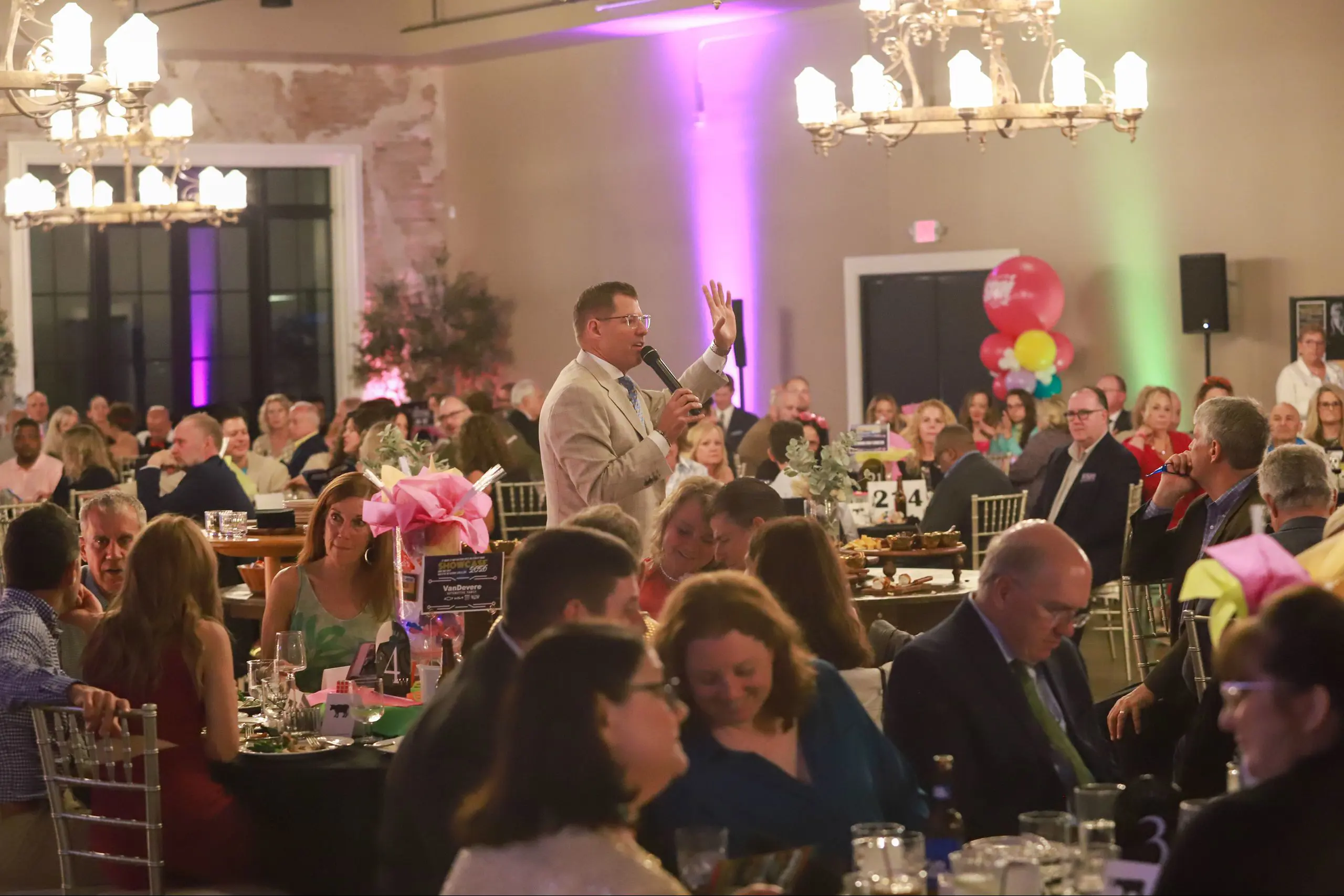 Guests at an STVM Showcase event sit at dining tables listening to a speaker.