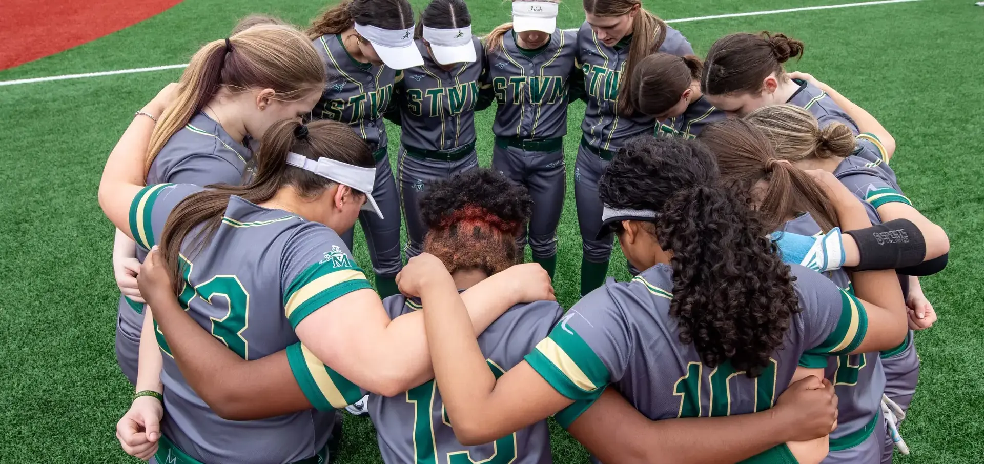 St Vincent St Mary High School softball team in a huddle on the pitch.